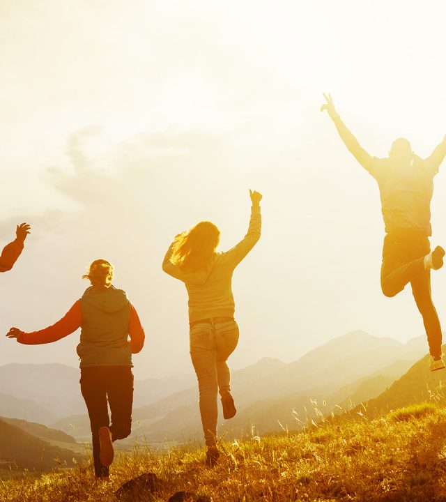 Group of five happy friends is running and jumping in sunset light on background of mountains. Happiness and friendship concept